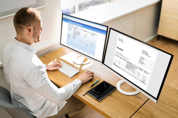 Young Businessman Looking At Invoice While Doing Online Banking On Computer